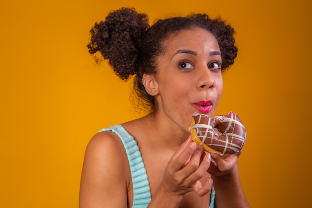 Młoda kobieta afro jedzenie pyszne pączki czekoladowe.