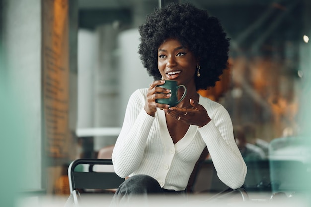 Młoda kobieta afro robi sobie przerwę i pije kawę w kawiarni