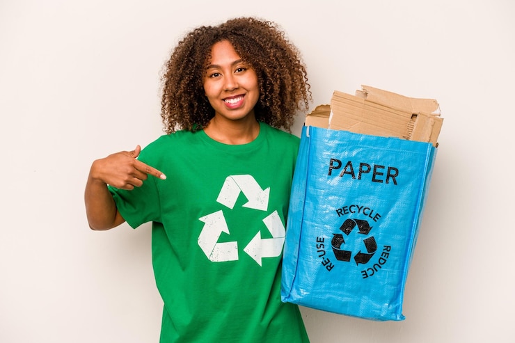 Zdjęcie młoda kobieta afroamerykanka trzymająca torbę do recyklingu pełną papieru do recyklingu na białym tle osoba wskazująca ręcznie na koszulkę kopia przestrzeń dumna i pewna siebie