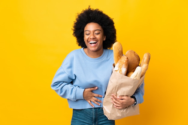 Młoda Kobieta Afroamerykanów Kupując Coś Chleb Na żółtym Tle Uśmiecha Się Dużo