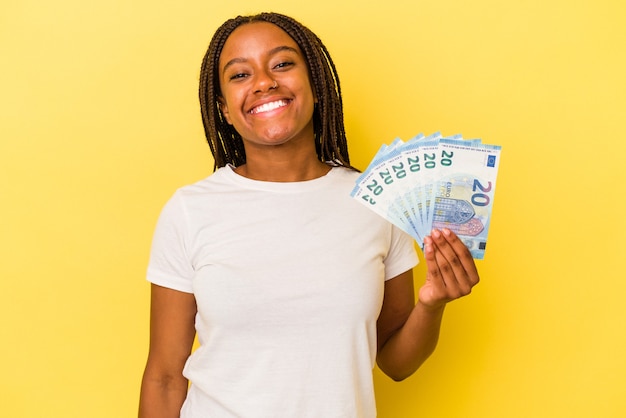 Młoda kobieta Afroamerykanów posiadających rachunki na białym tle na żółtym tle szczęśliwa, uśmiechnięta i pogodna.