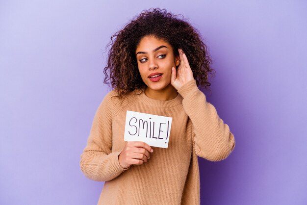 Młoda Kobieta Afroamerykanów Trzyma Tabliczkę Smile Na Fioletowej ścianie, Próbując Słuchać Plotek