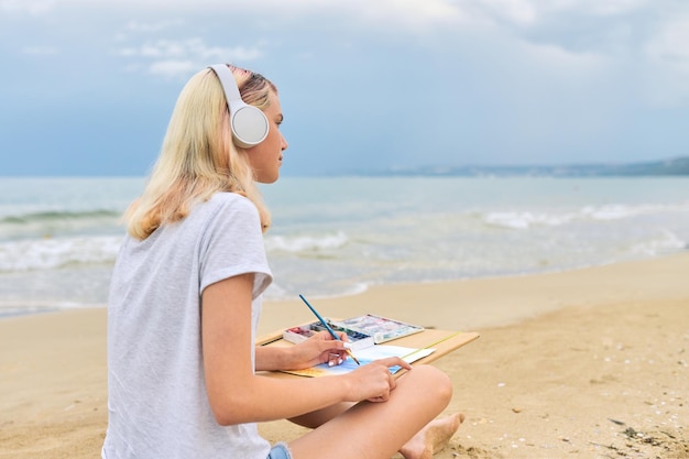 Młoda kobieta artysty malująca akwarelami siedząca nad brzegiem morza