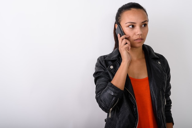 młoda kobieta Azji rozmawia przez telefon komórkowy, mając na sobie skórzaną kurtkę przed białą przestrzenią