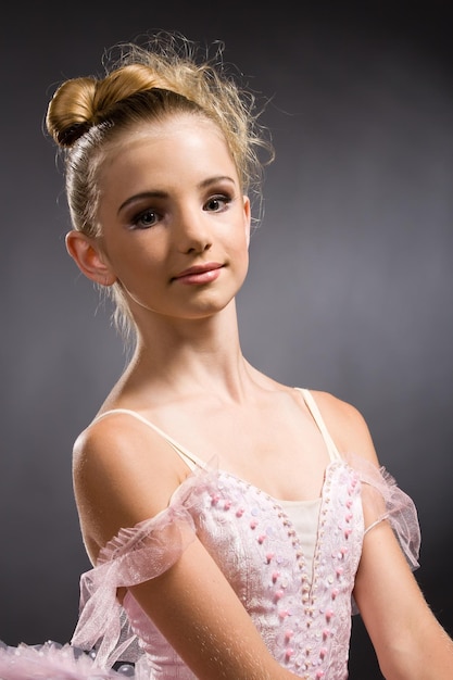 Młoda kobieta balerina w białej tutu tańczy na pointe z rękami nad głową w studio na ciemnym tle