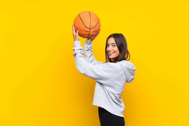 Młoda kobieta bawić się koszykówkę nad odosobnioną kolor żółty ścianą