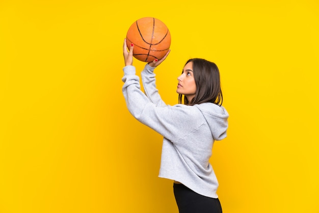 Młoda kobieta bawić się koszykówkę odizolowywającą na kolorze żółtym