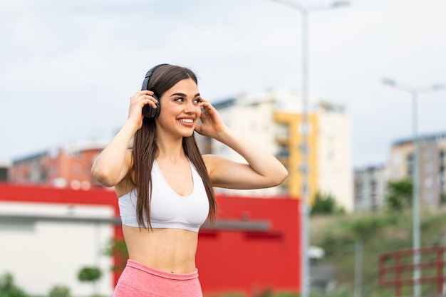 Młoda kobieta biegacz słucha muzyka na słuchawkach. Dopasuj sportsmenkę odpoczywając od treningu na świeżym powietrzu.