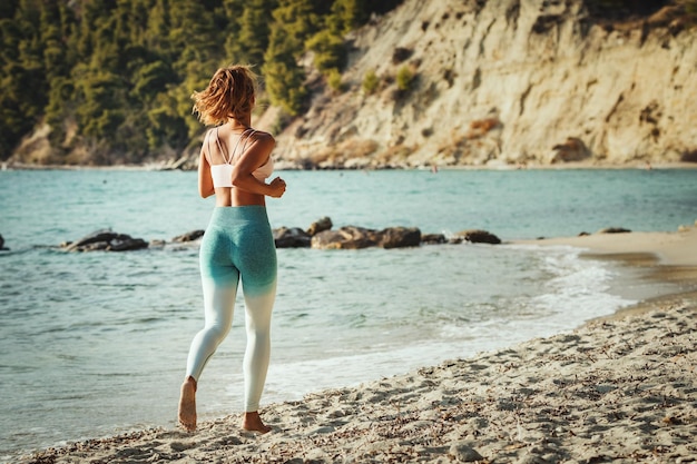 Młoda kobieta biegnie wzdłuż brzegu morza na plaży w upalny dzień wakacji.