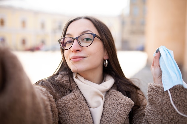 Młoda kobieta bierze selfie Kobieta pokazuje maskę medyczną do aparatu Kobieta w okularach dla wzroku