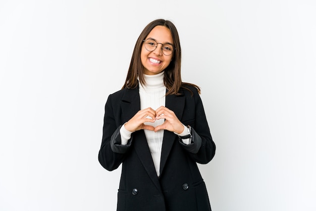 Młoda kobieta biznesu na białym tle na białej ścianie, uśmiechając się i pokazując kształt serca rękami