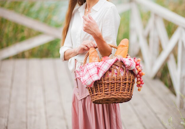 Młoda kobieta blondynka z długimi włosami w stylu retro vintage ubrania stoi z kosz piknikowy na drewnianym molo nad jeziorem