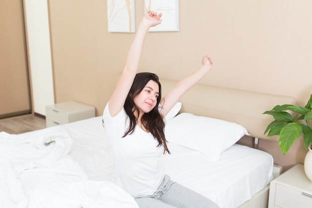 Młoda kobieta budzi się i podnosi ręce na łóżku w hotelowej sypialni