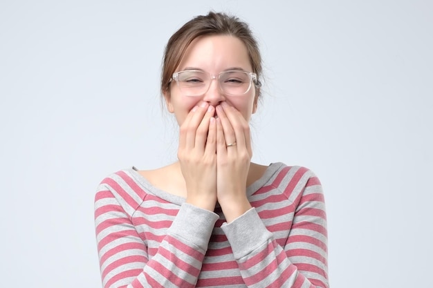 Młoda kobieta chichocze radośnie zakrywa usta, próbując przestać się śmiać