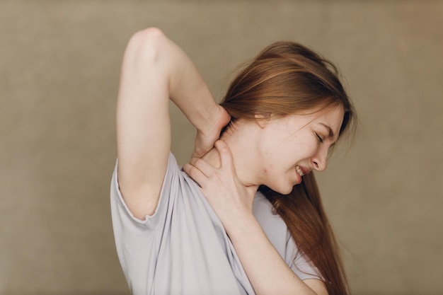Młoda kobieta cierpi na ból górnej części szyi na brązowym tle