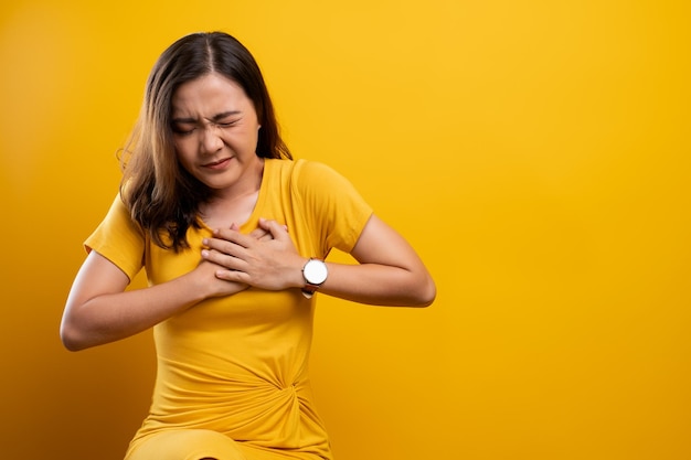 Młoda kobieta cierpiąca na ból klatki piersiowej siedząca na żółtym tle