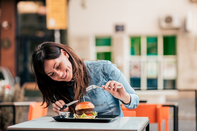 Młoda kobieta cieszy się wyśmienicie hamburger.