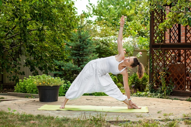 Młoda kobieta ćwiczy jogę na dziedzińcu wiejskiego domuTriangle pose triconasana