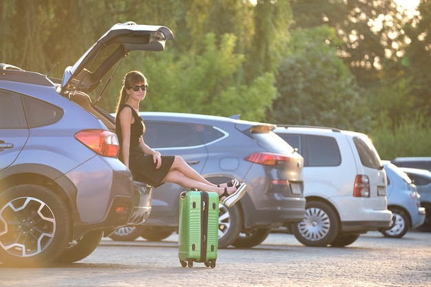 Młoda kobieta czeka obok samochodu z walizkową torbą. Koncepcja podróży i wakacji.