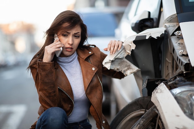 Zdjęcie młoda kobieta czuje się zrozpaczona po wypadku samochodowym i wzywa pomoc drogową przez telefon komórkowy