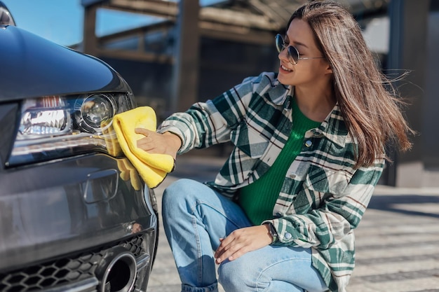 Młoda kobieta czyści i poleruje swój samochód żółtą ściereczką z mikrofibry Koncepcja dbania o samochód