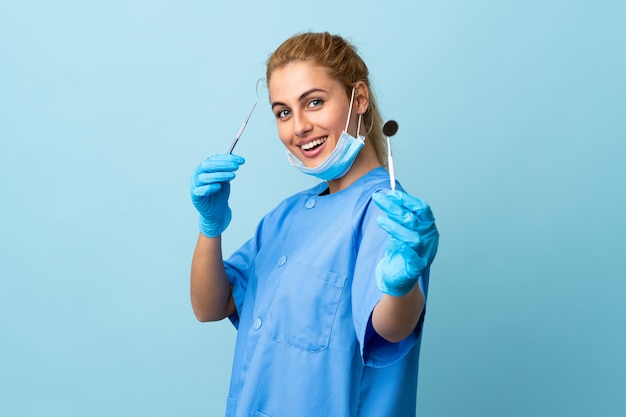 Młoda kobieta dentysty mienia narzędzia nad błękit ścianą