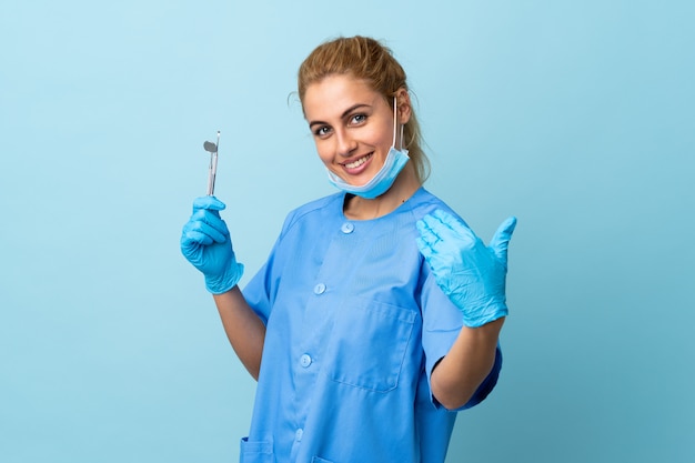 Młoda kobieta dentysty mienia narzędzia nad odosobnionym błękitnym zaprasza przychodzić