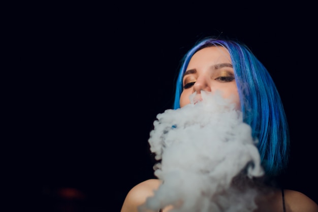 Młoda kobieta dymi elektronicznego papieros przeciw czarnemu tłu