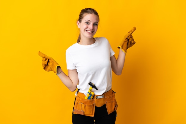 Młoda kobieta elektryk na białym tle na żółtej ścianie, wskazując palcem na boczne i szczęśliwa