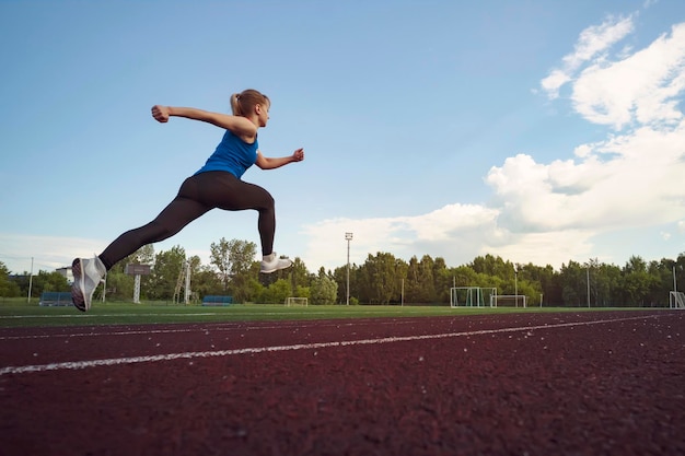 Młoda kobieta fitness biegacz biegający po torze stadionowym Czas skoku w locie Lekkoatletyka Pojęcie zdrowego stylu życia i sportu