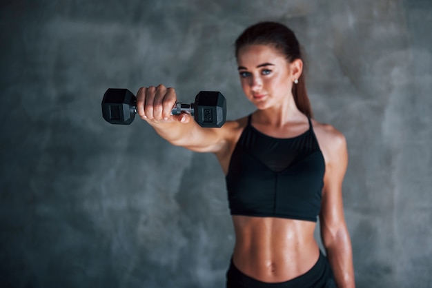Młoda kobieta fitness jest na siłowni w pobliżu ściany z hantlami w rękach.