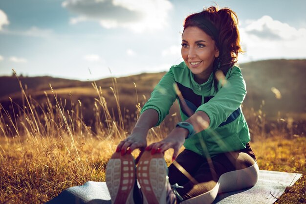 Młoda kobieta fitness robi ćwiczenia rozciągające po joggingu w naturze.