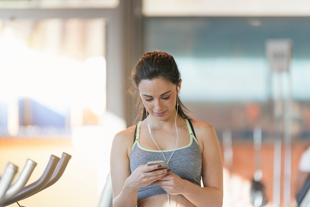 Młoda kobieta fitness szuka telefonu na siłowni. Koncepcja sportu.