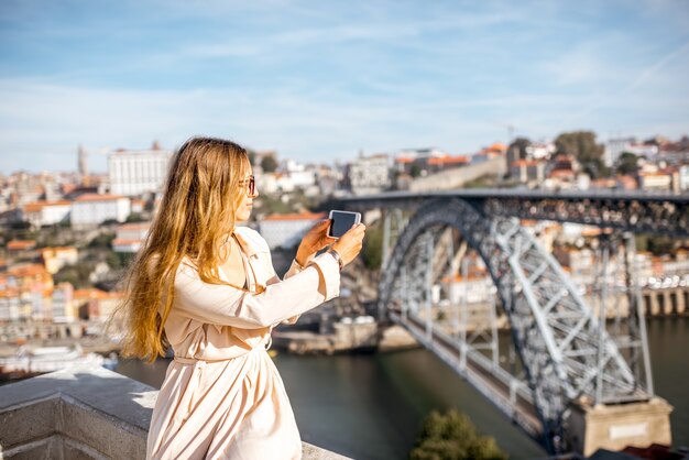 Młoda kobieta fotografująca telefonem piękny widok na panoramę miasta ze słynnym żelaznym mostem w mieście Porto, Portugalia