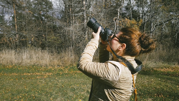 Zdjęcie młoda kobieta fotografuje przez kamerę, stojąc w lesie