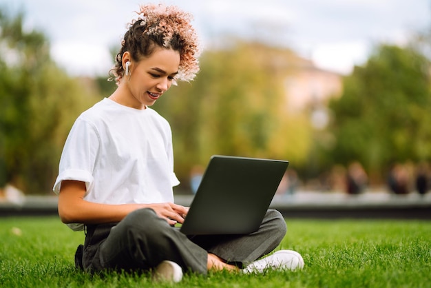 Młoda kobieta freelancer lubi oglądać seminarium edukacyjne na laptopie siedzącym na zielonej trawie