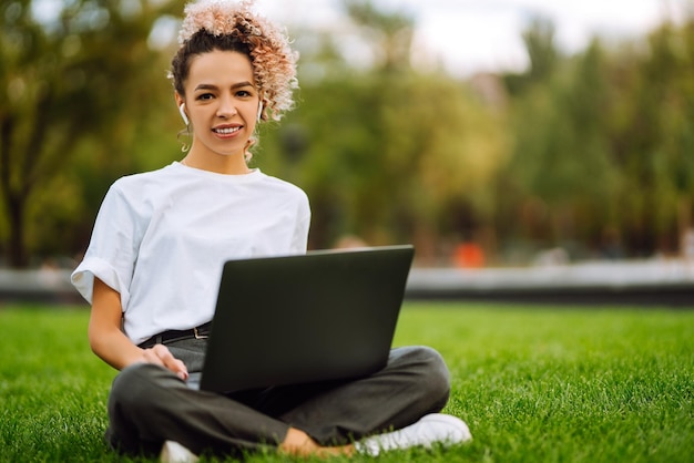 Młoda kobieta freelancer lubi oglądać seminarium edukacyjne na laptopie siedzącym na zielonej trawie