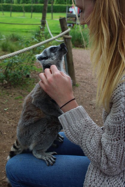 Zdjęcie młoda kobieta głaskająca lemura siedząc na polu w parku