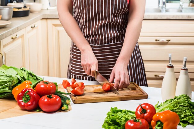 Młoda kobieta gotowanie w kuchni w domu. Zdrowe jedzenie. Dieta. Koncepcja diety. Zdrowy tryb życia. Gotowanie w domu. Przygotuj jedzenie. Kobieta kroi nożem pomidora i warzywa.