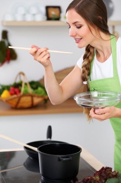 Młoda kobieta gotuje w kuchni Gospodyni domowa smakuje zupę drewnianą łyżką
