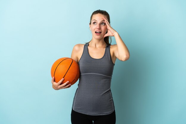 Młoda kobieta gra w koszykówkę na białym tle na niebiesko robi gest niespodzianki, patrząc w bok
