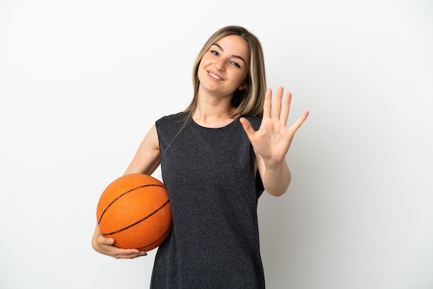 Młoda kobieta gra w koszykówkę nad odosobnioną białą ścianą, licząc pięć palcami