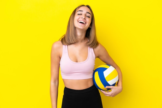 Młoda kobieta gra w siatkówkę na żółtym tle śmiejąc się