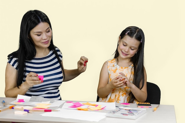 Młoda kobieta i jej córeczka robią wycinanki z papieru i rysują razem na pastelach