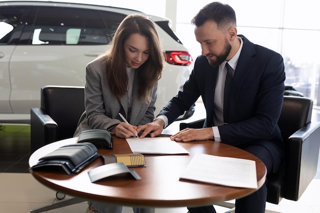 Młoda kobieta i kierownik sprzedaży samochodów podpisują umowę