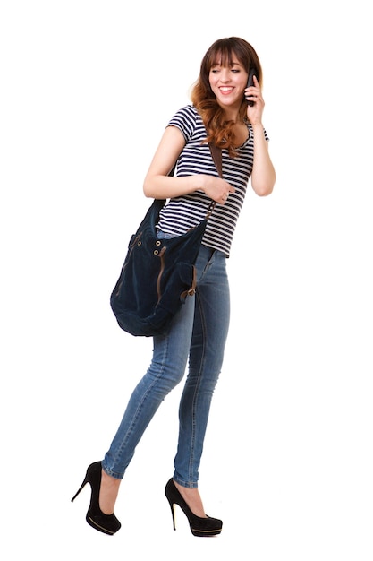 Młoda kobieta idąca na białym tle z telefonem komórkowym i torebką
