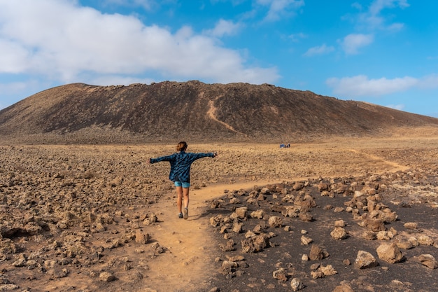 Młoda kobieta idąca ścieżką do krateru wulkanu Calderon Hondo w pobliżu Corralejo, północne wybrzeże wyspy Fuerteventura, Wyspy Kanaryjskie. Hiszpania