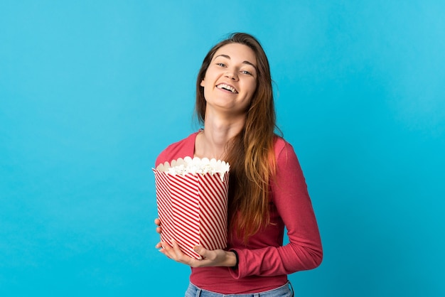 Młoda kobieta Irlandii na białym tle na niebieskim tle trzyma duże wiadro popcorns