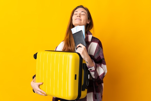 Młoda kobieta Irlandii na białym tle na żółtym tle w wakacje z walizką i paszportem