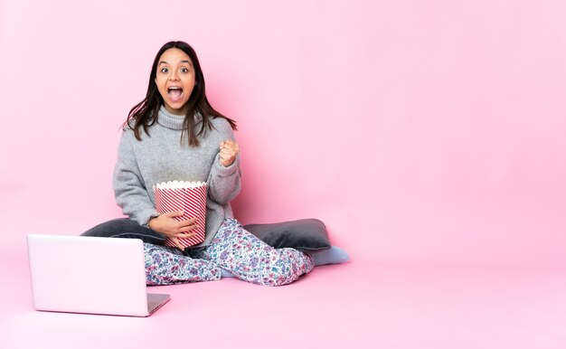 Młoda kobieta je popcorn podczas oglądania filmu na laptopie świętuje zwycięstwo w pozycji zwycięzcy